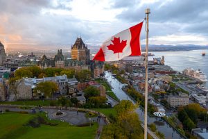 A flowing Canadian flag on a flagpole. Taken at sunset with Old Quebec City and the St. Lawrence River in the background. Aerial HDR view.